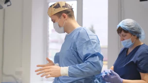Sebész Műtétre Készül Egy Mentős Segít Felvenni Egy Orvosi Köpenyt — Stock videók