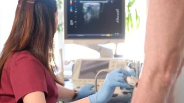 Doktor hastaların bacaklarına ultrason uygular. Yaşlı bir kadın bir klinikte ultrason muayenesinden geçiyor. 4k video