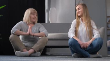 Büyükanne ve kızı evde, oturma odasının ortasında yerde otururken yoga yapıyorlar. Sağlıklı Yaşam Tarzı