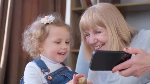 Egy Aranyos Kisgyerek Nagymamája Otthon Ülnek Kanapén Szórakozást Okostelefon Nézegetéséhez — Stock videók