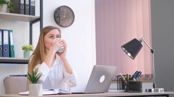 昼休みにオフィスのパソコンに座っていると 若い女性管理者がお茶を飲みます ビジネス女性のための昼食休憩 — ストック動画