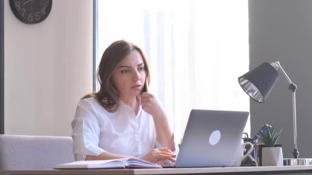一位穿着正式西装的女商人坐在公司总部的办公桌前 一边打电话一边聊天 在笔记本电脑上工作的女商人 — 图库视频影像