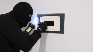 Siyah maskeli bir erkek yankesici alet kullanarak bir apartman kasasını açıyor. Kanunun ihlali.