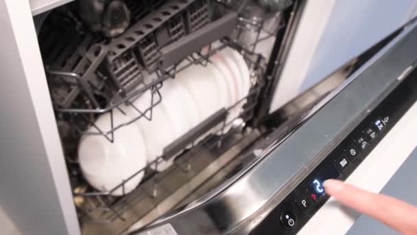 一名妇女按下自动洗碗机的按钮启动程序 装洗碗机 — 图库视频影像