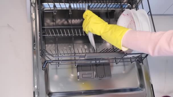 ゴム手袋のビデオ女性の手は食器洗い機に白いプレートを置きます 現代的なキッチンで汚れた料理の自動洗浄 — ストック動画