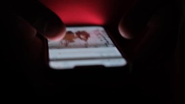 Erkek el, karanlık ışıkta parmaklarıyla akıllı telefon ekranında çalışır. İnternetten bilgi aranıyor. Akıllı telefondan video izliyorum..