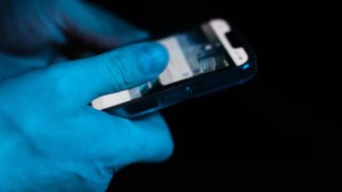 Bir adamın eli parmaklarını hızlı bir şekilde akıllı telefonun ekranında hareket ettirir ve internette bir şeyler arar. Mavi ışıkta akıllı telefonu olan bir erkek.