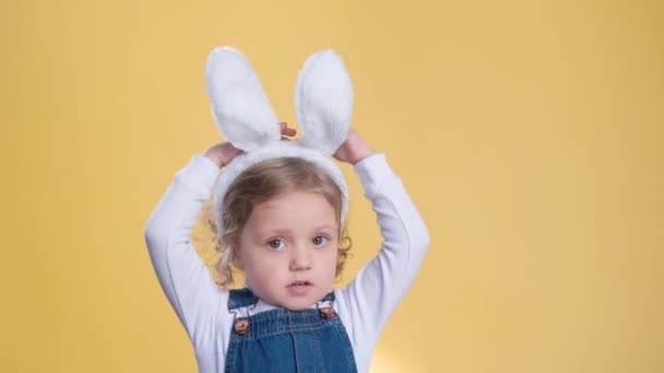 一个有着黄色背景的复活节兔子耳朵的可爱小女孩表现出不同的情感 快乐和梦想 — 图库视频影像