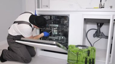 Üniformalı tamirci mutfaktaki bulaşık makinesini tamir ediyor. Tamirci bulaşık makinası mutfakta..