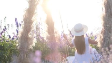 Beyazlar içinde genç bir bayan bir tarlanın ortasında salıncakta sallanıyor. Güzelliğin tadını çıkar. Lavanta renkli fotoğraf oturumu.