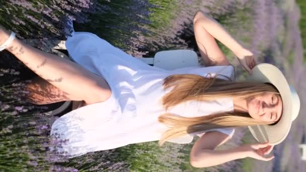 一个穿着白色风格的美女坐在薰衣草地里享受阳光的垂直录像 一个女人在薰衣草里摆姿势 — 图库视频影像