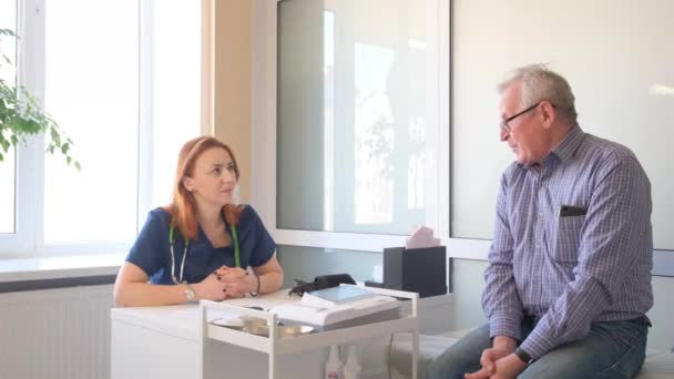 Una Doctora Sienta Escritorio Habla Con Paciente Anciano Mientras Observa — Vídeos de Stock