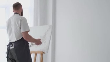 Sanatçı alçı kullanarak beyaz bir tuval üzerinde bir resim yaratıyor. Bir sanatçının soyut bir resim yapma süreci