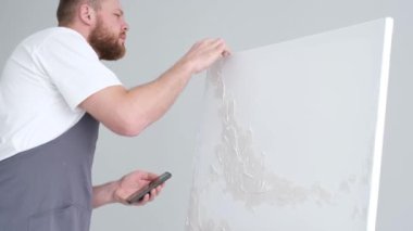 Yetenekli bir erkek sanatçı, fırça kullanarak, beyaz bir tuvalde yağlı boya tablosunun modern bir başyapıtını yaratıyor. Tuval büyük bir stüdyoda bir sehpanın üzerinde..