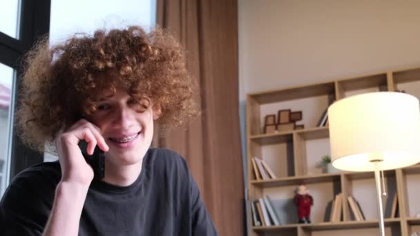 一个留着奇怪发型的年轻人在讲电话 快乐的卷曲红头发的年轻人在讲电话 技术和通信 — 图库视频影像