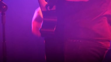 Bir müzisyen sahnede bir konser sırasında akustik gitar çalar. Müziğini vurgulamak için boncuk, ton ve ses kontrolü ve gitar efektörü kullanıyor.