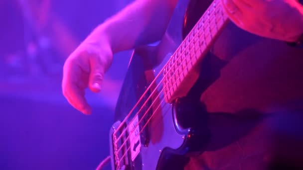クラブのロック コンサートでエレキ ベースのギターを弾いている男性ギタリストのクローズアップ 赤と青の照明 — ストック動画