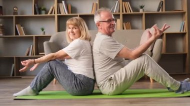 Arka planda kitaplar olan güzel bir odada halıya oturmuş meditasyon yapan mutlu yaşlı çift. Yaşlıların sağlıklı yaşam tarzı