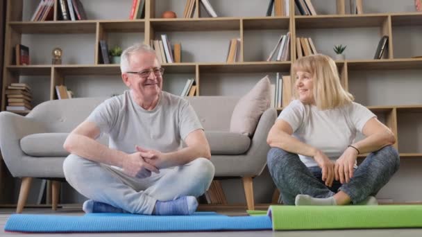 ヨガをしながら話す満足したシニア男女 自宅でヨガのクラス 高齢者の健康的な生活様式 — ストック動画