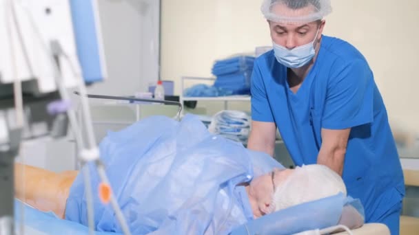 一位外科医生与躺在手术台上的一位老年病人交谈 病人正处于麻醉状态 爷爷在手术室里 — 图库视频影像