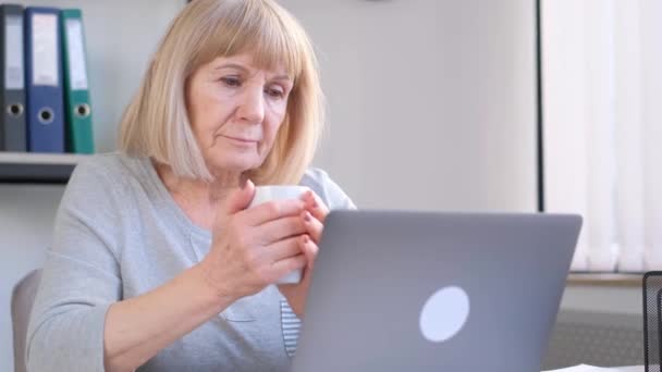 おばあちゃんはビデオリンクを介して通信し 手にお茶のマグカップを持っています 古い時代の近代技術の使用 — ストック動画