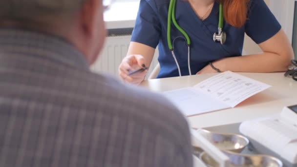 一位女医生坐在她的办公桌前 一边与一位老年病人交谈 一边看他的测试结果 心脏病医生会咨询办公室里的人 — 图库视频影像