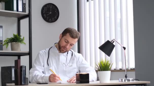 一个年轻英俊的兽医的画像坐在一个有现代内饰的兽医诊所的桌子旁 写着什么 兽医在工作 — 图库视频影像