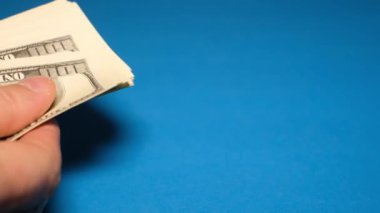 Bir adam mavi arka planda yüz dolarlık banknotlar sayar. Yakın plan para sayıyorum. Kağıt para, ödeme, servet, yatırım satın almak.