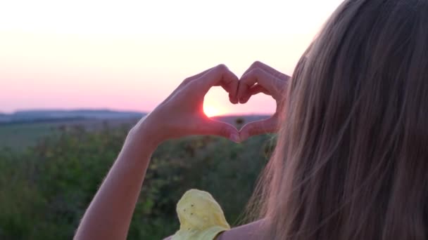 若い女性が畑の美しい夕日に手を合わせて心のジェスチャーをします 4Kビデオ — ストック動画
