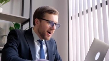 Ofiste neşeli bir işadamı, laptopta harika haberler var. Kazanan adam, finansal piyasa büyüme konseptini kutlayan bir ödül aldıktan sonra mutlu hissediyor. 4k video