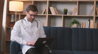 Beyaz önlüklü bir doktor evde oturma odasında çalışıyor, e-postalarını okuyor. Bir doktor hasta hastalarla internet sohbetinde iletişim kurar.. 