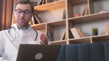 Beyaz önlüklü genç bir erkek doktor uzaktan video görüşmesi yapıyor ve hasta bir hastaya danışıyor. İnternet sohbetinde hastaya danışmanlık yaparken doktor kamerayla konuşuyor. 4k video