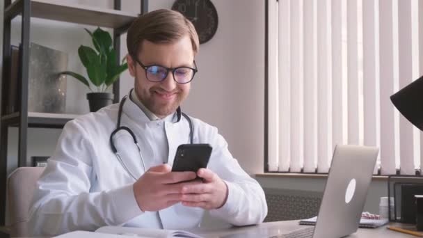 Médico Masculino Sostiene Teléfono Inteligente Sus Manos Sienta Escritorio Lugar — Vídeos de Stock