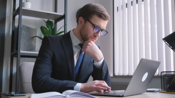 英俊的胡子经理 戴着眼镜 坐在办公室里 用他的笔记本电脑和电脑程式一起工作 — 图库视频影像