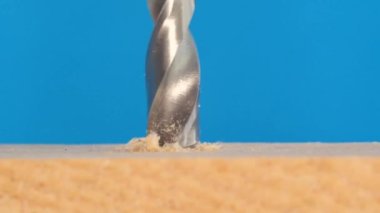 Güzel mavi bir arka planda metal matkapla ahşap bir yüzeye delik açmaya yakın plan. Elektrikli araçların makro videosu