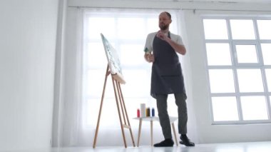 Mutlu bir sanatçı elinde fırçayla dans eder ve yağlı boya resminin modern bir başyapıtını yaratır. Stüdyoda soyut bir tablo yaratma süreci. 4k video