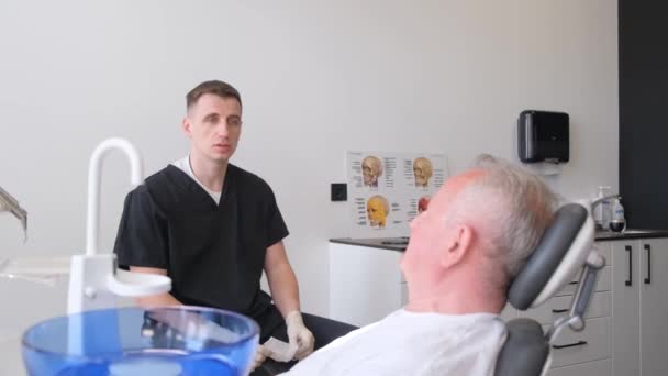 牙科医生旁边的一位年迈的老人坐在椅子上复述 上了年纪的男人坐在椅子上看牙医 — 图库视频影像