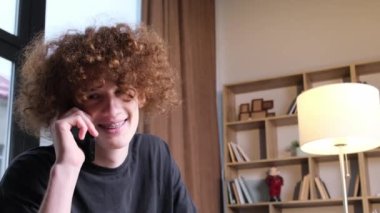 Garip saç stili olan genç bir adam telefonda konuşuyor. Telefonda konuşan kıvırcık saçlı mutlu genç adam. Teknoloji ve iletişim.