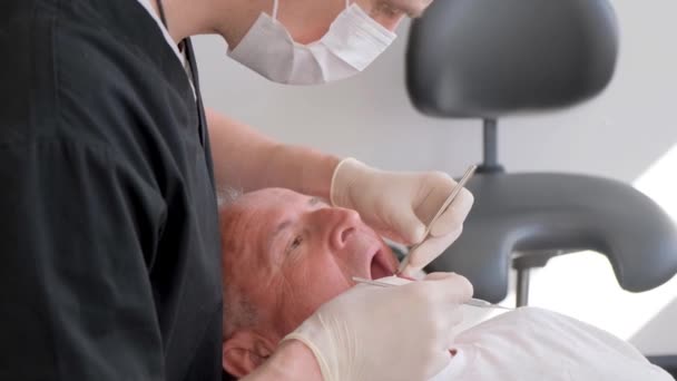 プロの歯科外科医が統一的に手術を行い 現代の計測器を備えたクリニックで高齢者の患者に歯科インプラントを設置します 4Kビデオ — ストック動画