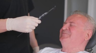 Bir cerrah yaşlı bir adamın önündedir ve yüzünde izler bırakır. Doktor yüzünde iz bırakmak için keçeli kalem kullanıyor ve onları estetik ameliyata hazırlıyor..