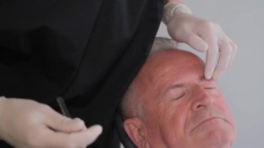 Yakın plan bir plastik cerrah yaşlı bir adamın gözünün altındaki kırışıklıkları inceler. Amerika 'da modern plastik cerrahi kliniği.
