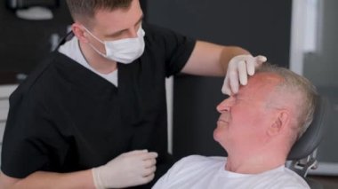 Yüzündeki işaretler için erkek blefaroplasti. Estetik cerrah, estetik ameliyattan önce göz bölgesini değiştirmek için yüzü inceler.