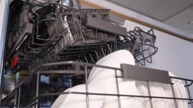 Eldiven takan bir kadın bulaşık makinesini çalıştırır. Bir sürü kirli mutfak malzemesi.