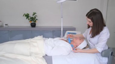 Modern bir kozmetoloji kliniğinde mikro akım tedavisini kullanarak cilt yenileme. Donanım kozmetolojisi. Güzellik salonunda bir kadının yüzüne bakmak