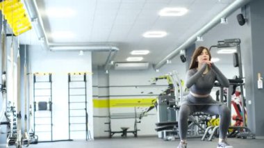 Genç Asyalı kız spor salonunda çömelerek bacak kaslarını çalıştırıyor. Kalça kaslarının çalışması. Güzel aktif kadın spor salonunda