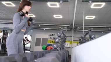 Kız spor salonunda dambılları kaldırıyor. Kalça kaslarının çalışması. Güzel bir atletik kadın figürü. Aktif kadın