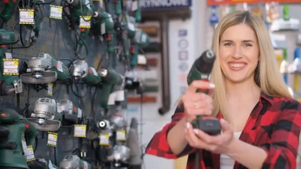 電動ドリルを持ってカメラを笑っている美しい販売の女の子の肖像 ハードウェアストアのプロモーションビデオ — ストック動画