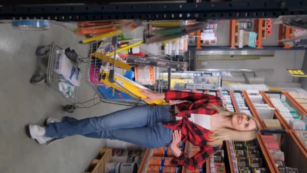 建材のカートと金物店で美しいブロンド 家の修理のための買い物 垂直ビデオ — ストック動画