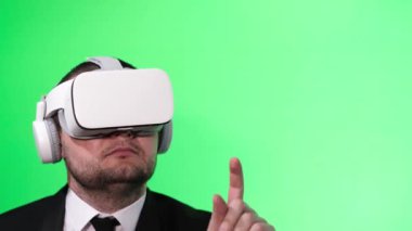 Stüdyoda yeşil arka planda sanal gerçeklik gözlüğü kullanan genç bir iş adamı..