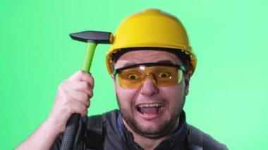 İnşaat işçisi çekiçle metal bir aletle saldırıyor. Krom arka planda üniformalı ve kasklı çılgın inşaat işçisi.